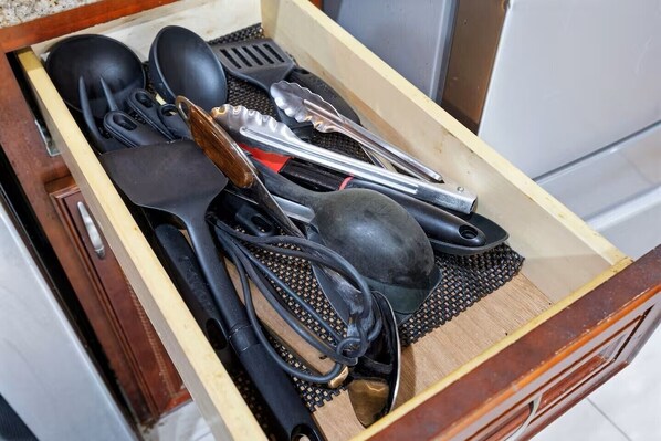 A drawer filled with kitchen utensils including tongs, a spatula, and a pot.