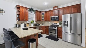 A modern kitchen with wooden cabinets, stainless steel appliances, a granite countertop, and a small island with bar stools.