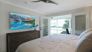 A bedroom with a large bed, a ceiling fan, a painting of a mountain landscape, a dresser, and a sliding glass door leading to a balcony. - Luxe Waterfront Condo on Longboat Key - Beach Breeze (Longboat Key)