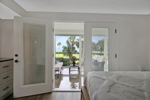 A bedroom with a large bed, a sliding glass door leading to a balcony with a view of palm trees and a lawn. - Luxe Waterfront Condo on Longboat Key with beach access - Beach Breeze (Longboat Key)