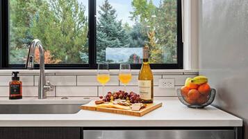 A kitchen counter with a wine bottle, glasses, fruit, and a hand soap bottle.