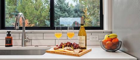 A kitchen counter with a wine bottle, glasses, fruit, and a hand soap bottle.