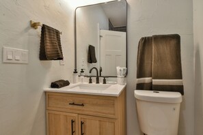 Ein Badezimmer mit einem weißen Waschbecken, Holzschränken, einem Spiegel und zwei Handtüchern, die an der Wand hängen.