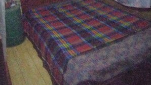A small, dimly lit room with a single bed, a bedside table, and a wall-mounted TV. - Cozy cabin up the hills (Medellín)