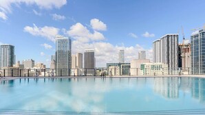 Un paisaje urbano con una amplia piscina tranquila en primer plano y rascacielos al fondo.