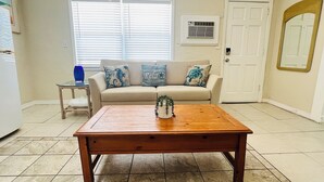 A living room with a wooden coffee table, beige sofa with patterned cushions, a small side table with a blue vase, and a white door. - Beach & Relaxation, 2BR, Family + Dog Friendly (Redington Shores)