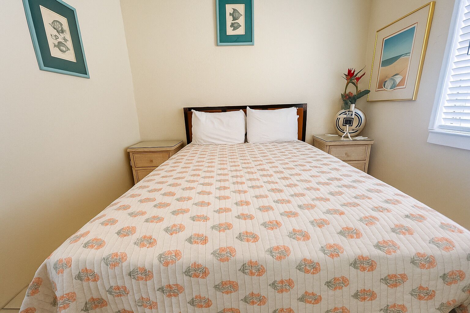 Una cama bien hecha con una colcha estampada con motivos florales, dos mesitas de noche con lámparas y cuadros enmarcados en las paredes.