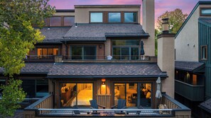 Une maison à plusieurs étages dotée d’un balcon, de grandes fenêtres et d’un intérieur visible, avec une cheminée.