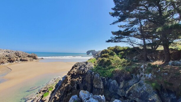 Un paysage côtier caractérisé par une côte rocheuse, une plage de sable et un ciel bleu dégagé.