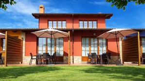 Un bâtiment à deux étages avec une façade rouge, de grandes fenêtres et un espace extérieur aménagé avec des parasols.