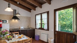 Une cuisine chaleureuse avec des poutres en bois, une table à manger dressée pour le petit-déjeuner et une fenêtre ornée de rideaux.