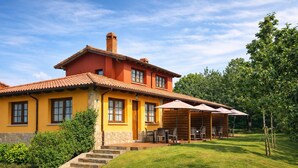 Une maison à deux étages, avec une façade jaune, un toit recouvert de tuiles rouges et un patio abrité doté de meubles pour se détendre en plein air.