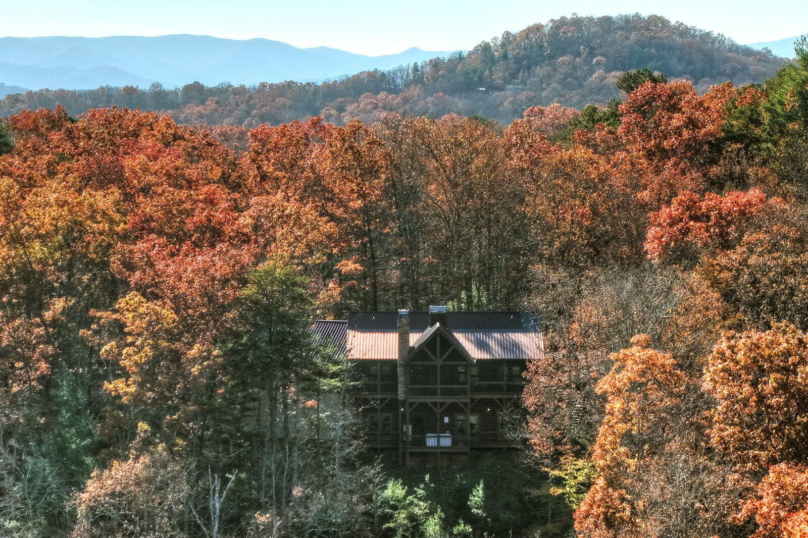 A cabin surrounded by autumn foliage with a mountainous backdrop.