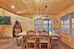 Un interior de madera con una mesa de comedor, sillas, una araña y una ventana con persianas.