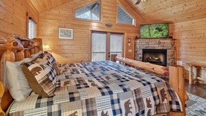 Une chambre confortable dans un chalet en rondins, avec un grand lit, une cheminée et un ventilateur de plafond.