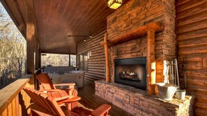 Une terrasse en bois avec des sièges d’extérieur, une cheminée en pierre et un jacuzzi.