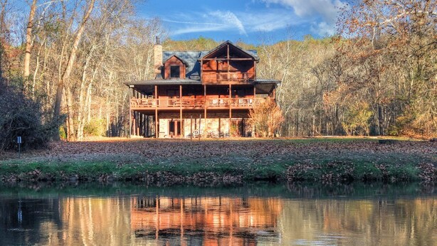 Une cabane dotée d’un balcon, entourée d’arbres et bordée par un plan d’eau.