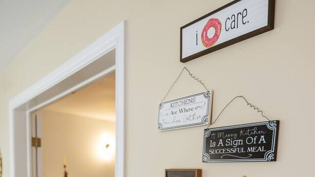 A kitchen area with a coffee maker on a wooden table, a Mickey Mouse-themed basket, and various kitchen signs on the wall. - Bright and Cozy Cottage in the Heart of Dartmouth (Dartmouth)