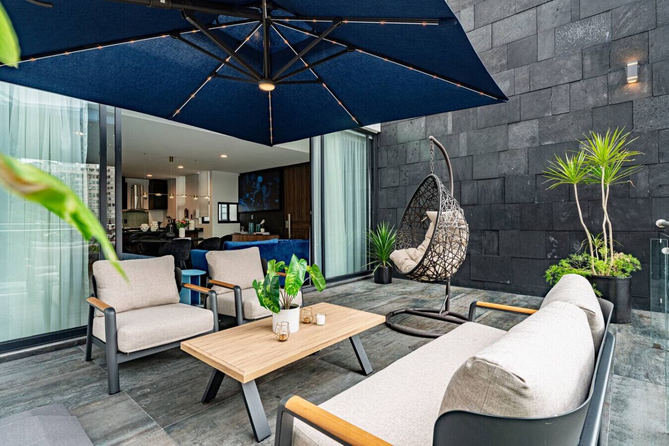 A modern outdoor seating area with a hanging chair, a wooden table, and a large umbrella.
