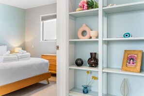 A hotel room with a bed, a nightstand, a window, and a shelf with decorative items.