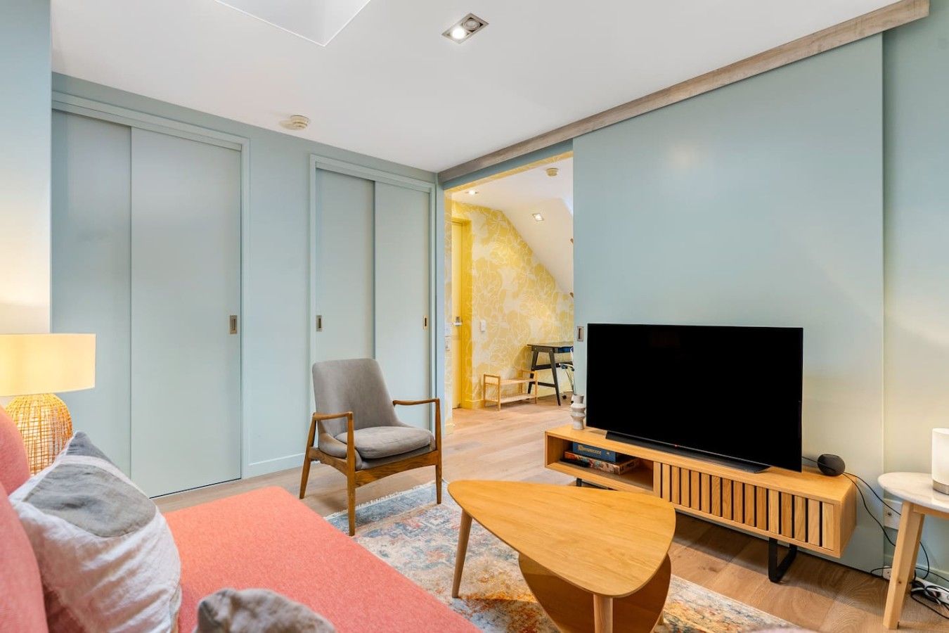 Un salon moderne avec un téléviseur à écran plat, une table basse en bois, un fauteuil gris et un canapé rose.