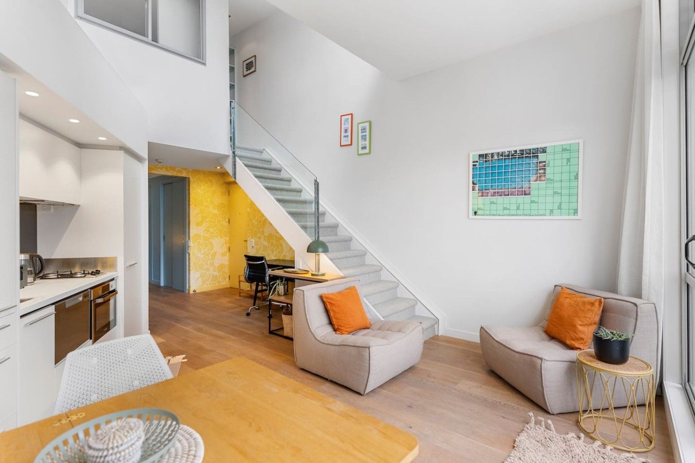 A modern interior with a kitchen, dining area, and seating space with a staircase.