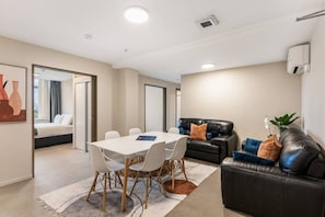 Una habitación de hotel moderna con zona de comedor, un sofá de cuero negro y una mesa blanca.