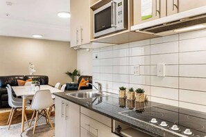 A modern kitchen with a microwave, sink, and stove. There is a dining area with a table and chairs. - A four bedroom apartment in Auckland CBD w Carpark (Auckland City)