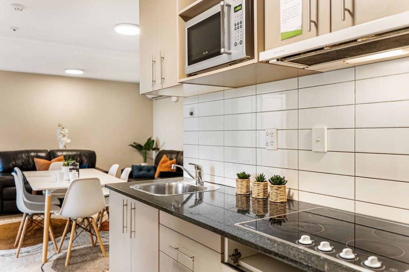 A modern kitchen with a built-in microwave, a sink, and a stove. There is a dining area with a table and chairs.