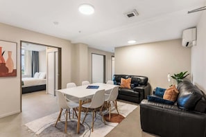 A modern hotel room with a dining area, a black leather sofa, and a large mirror.