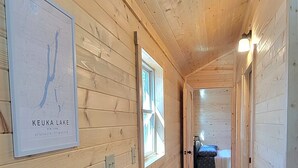 Un corridoio in legno con una mappa incorniciata a sinistra, che conduce a una camera da letto con un letto e una finestra.