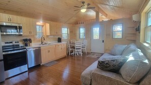Una cucina in stile baita con mobili in legno, frigorifero, fornello e microonde. C'è una zona pranzo con tavolo e sedie, e un divano con cuscini.