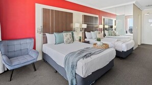 Ein Hotelzimmer mit zwei Betten, einem grauen Sessel und einem großen Spiegel.