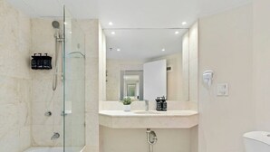 Ein modernes Badezimmer mit einer gläsernen Duschkabine, einem weißen Waschbecken, einem Spiegel und einer Toilette.