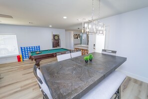 Un salon moderne avec une table de billard, un coin repas doté d’un grand îlot central et un lustre.