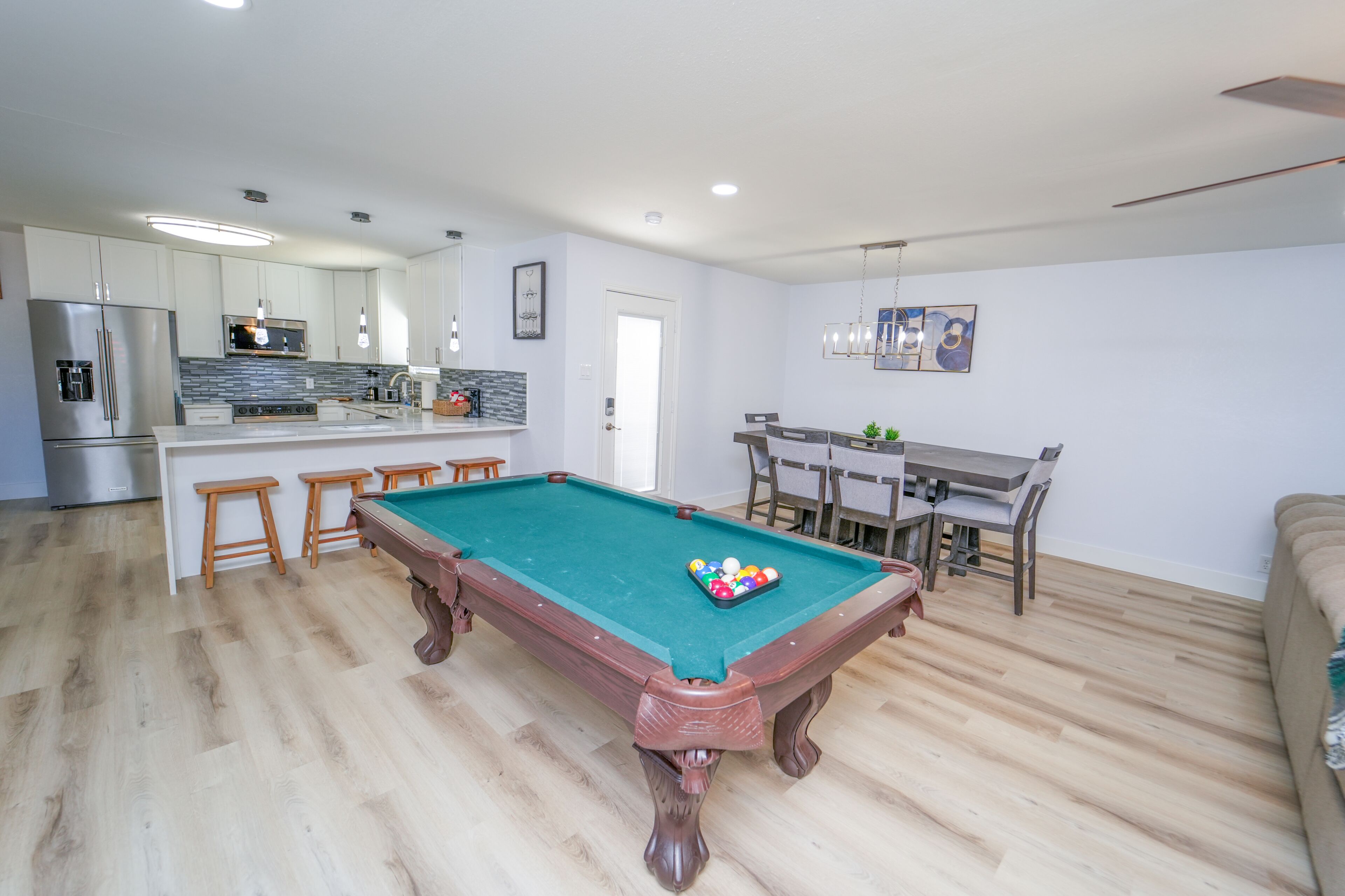 Une cuisine moderne avec un billard, des tabourets en bois et un coin repas comprenant une table et des chaises.