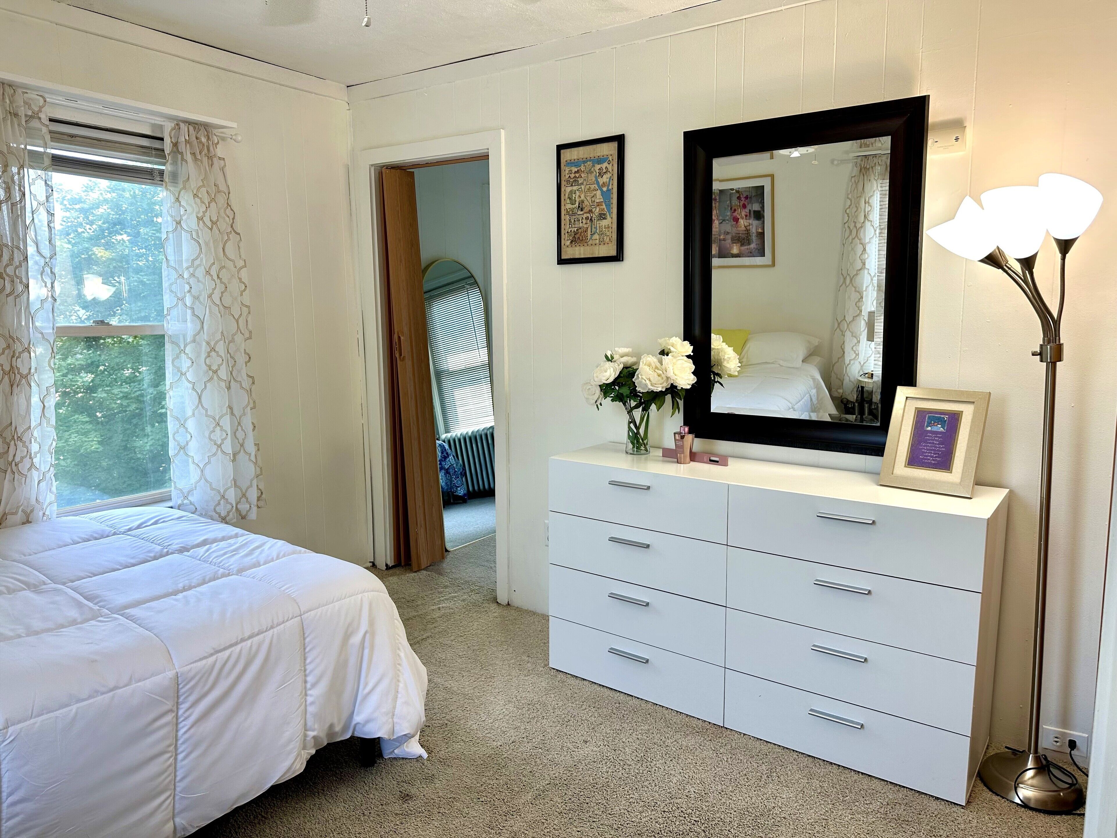 A bedroom with a bed, a dresser with drawers, a mirror, and a vase with flowers.