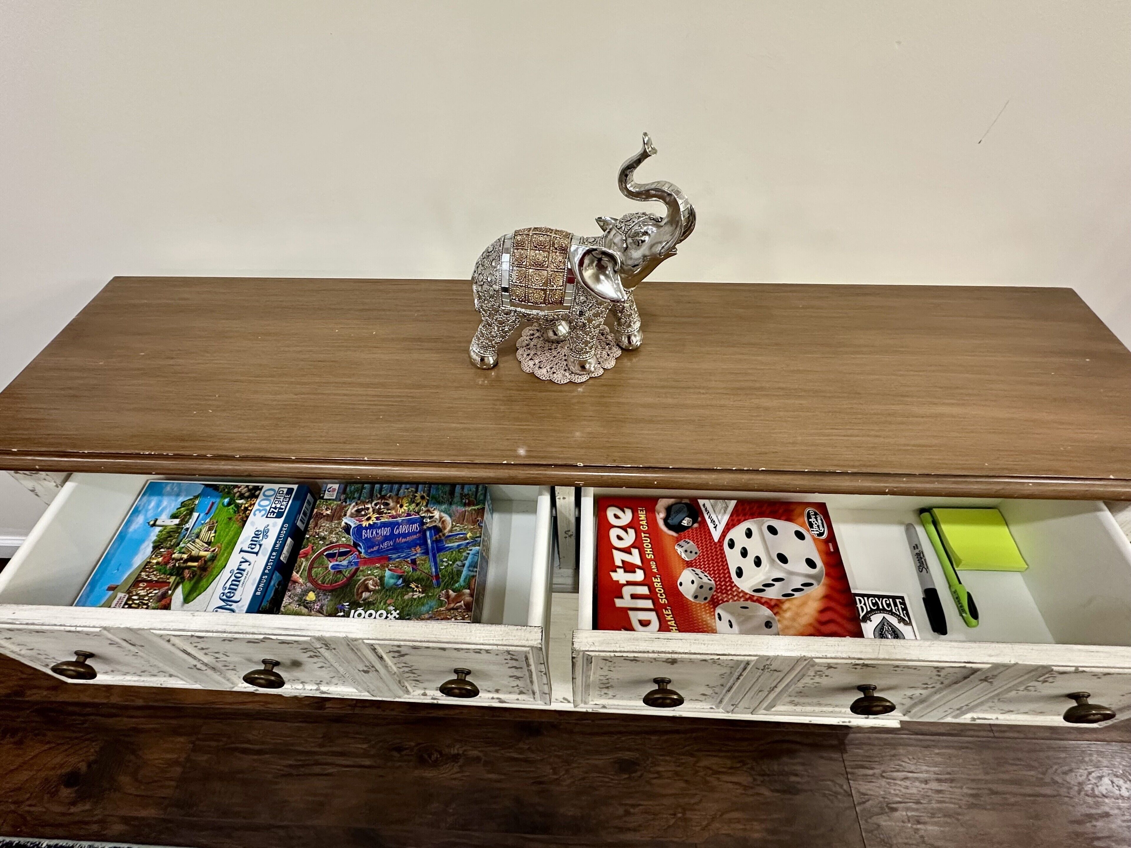 Ein Holztisch mit einer dekorativen Elefantfigur obenauf. Darunter befinden sich zwei offene Schubladen mit Gesellschaftsspielen und einem Würfelspiel.
