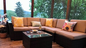 Un espace de détente extérieur accueillant, avec un canapé d’angle, une table basse en verre et une petite table d’appoint en osier.