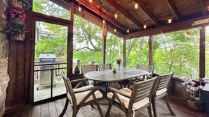 Un espace extérieur abrité, aménagé pour les repas, avec une table ronde et des chaises, des poutres en bois et des guirlandes lumineuses.