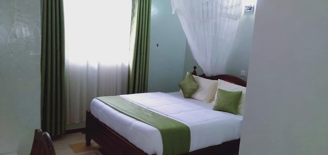 A neatly made bed with a green and white bedspread, two pillows, and a wooden headboard.
