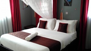 A double bed with white and red bedding, a rolled towel, and a mosquito net.