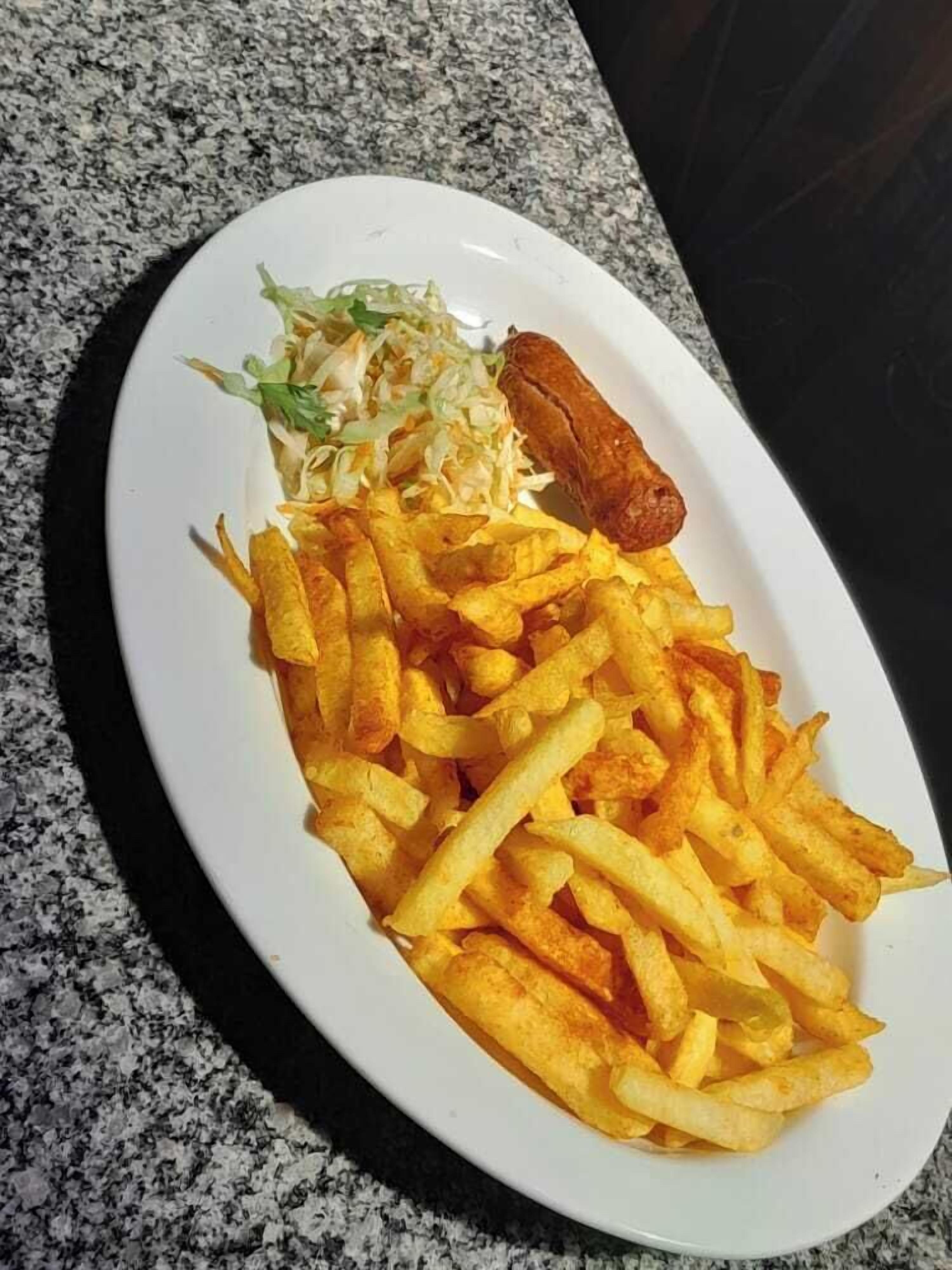 A plate of French fries, coleslaw, and a sausage on a granite countertop.