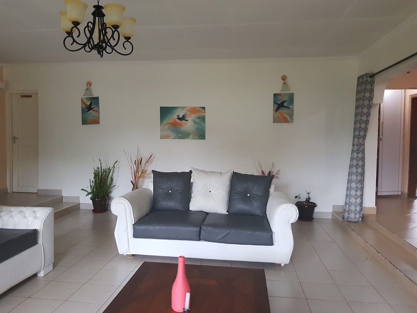 Una sala de estar con un sofá blanco, un jarrón rojo sobre una mesa de centro de madera y pinturas abstractas en las paredes.