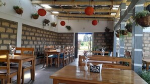 A rustic dining area with wooden tables and benches, stone walls, and hanging planters.