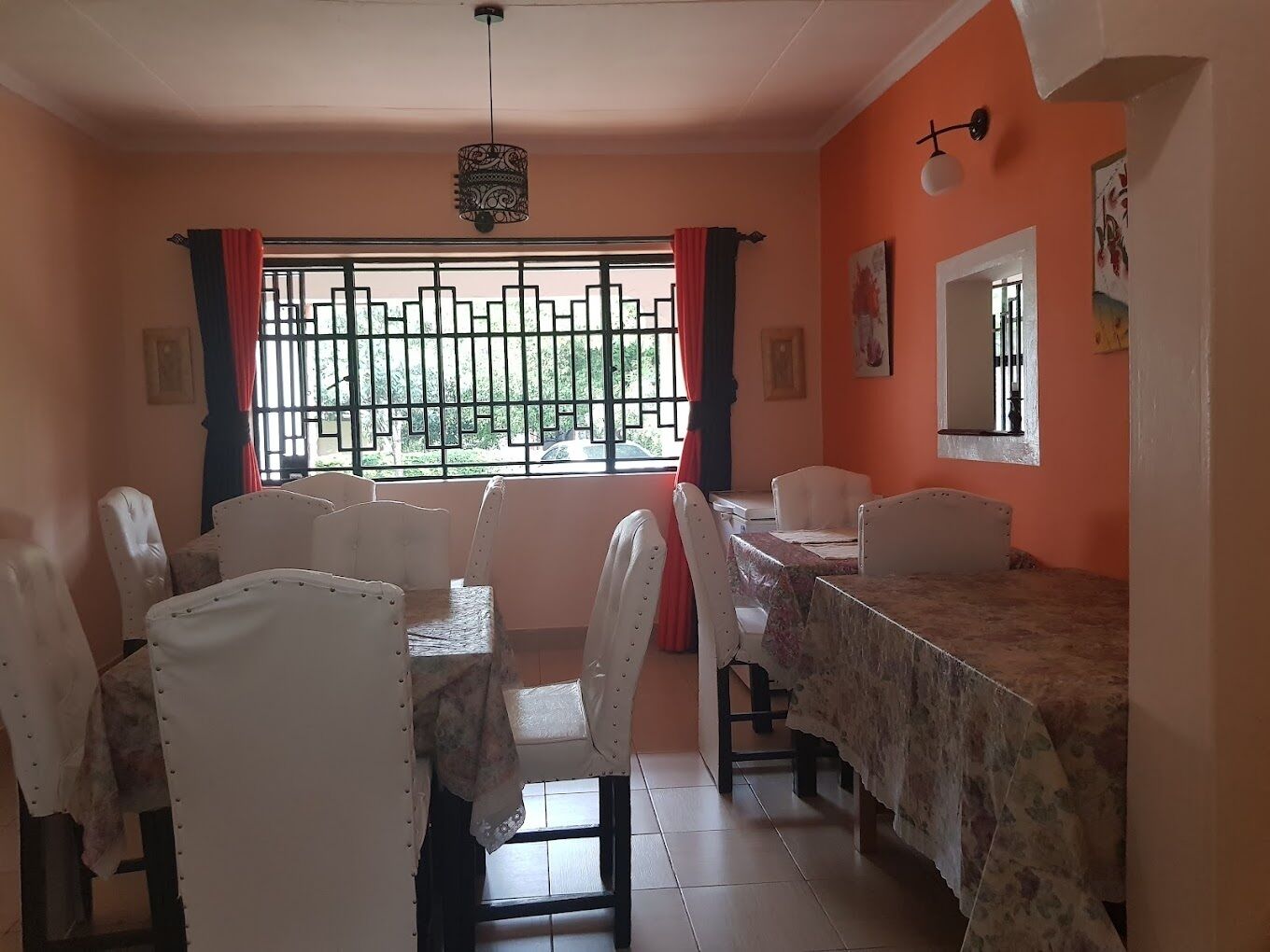 Un área de comedor con una mesa y sillas, una ventana con reja de metal y una lámpara fijada a la pared.