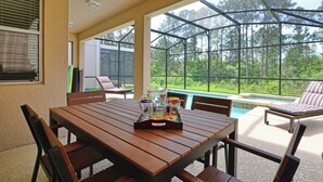 Um alpendre coberto com uma mesa de madeira, cadeiras e piscina.