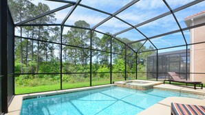 Piscina com cobertura de vidro, rodeada por um terraço com espreguiçadeiras e vista para uma área arborizada.