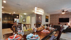 Uma sala de jantar com uma mesa comprida posta para seis pessoas, rodeada por cadeiras de madeira escura.