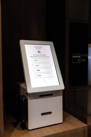 Un quiosco de autoservicio con pantalla táctil, opciones para seleccionar idioma y un símbolo de pago.